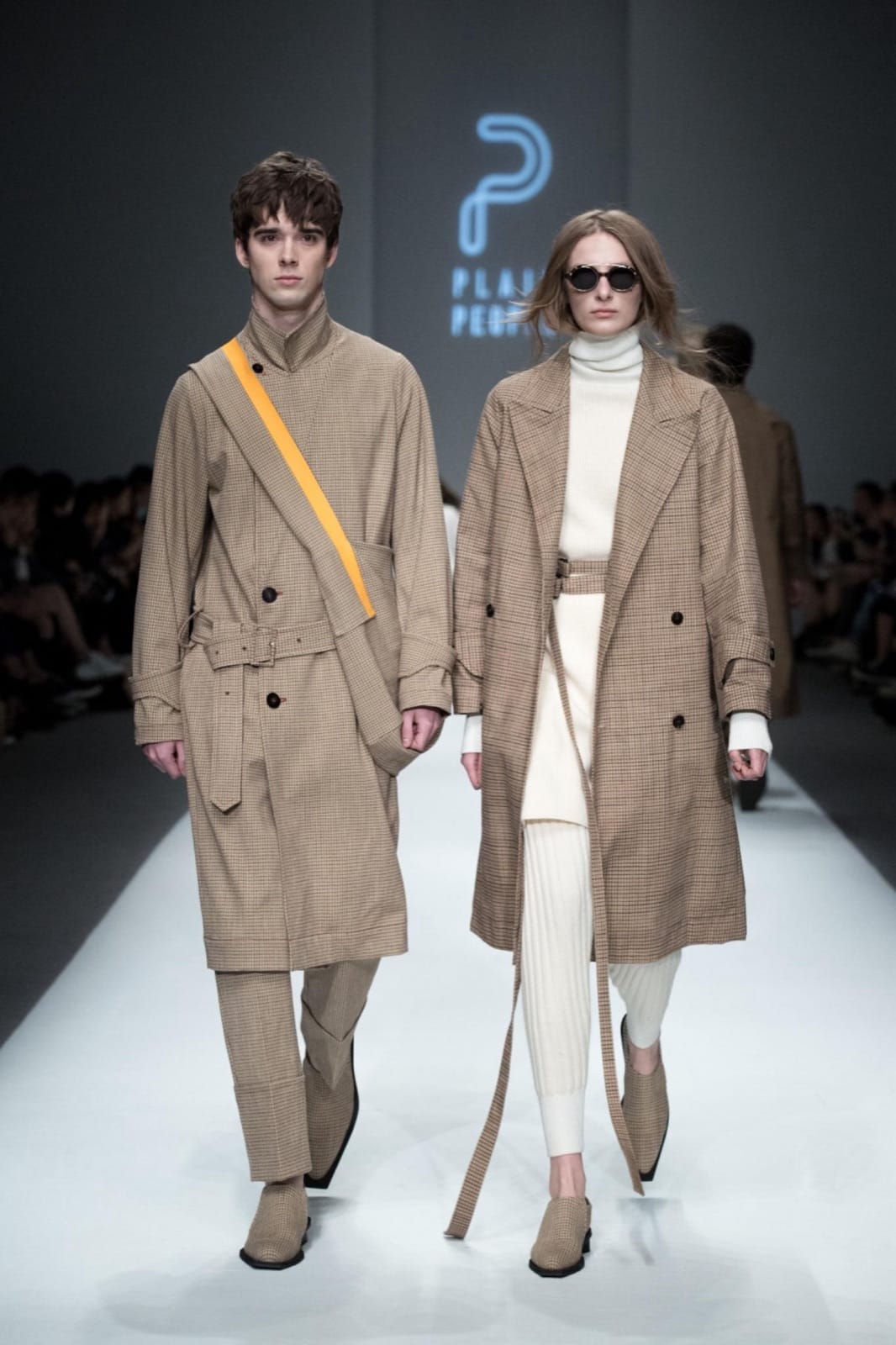 Vojtech Babista walking a runway show in a check trench coat